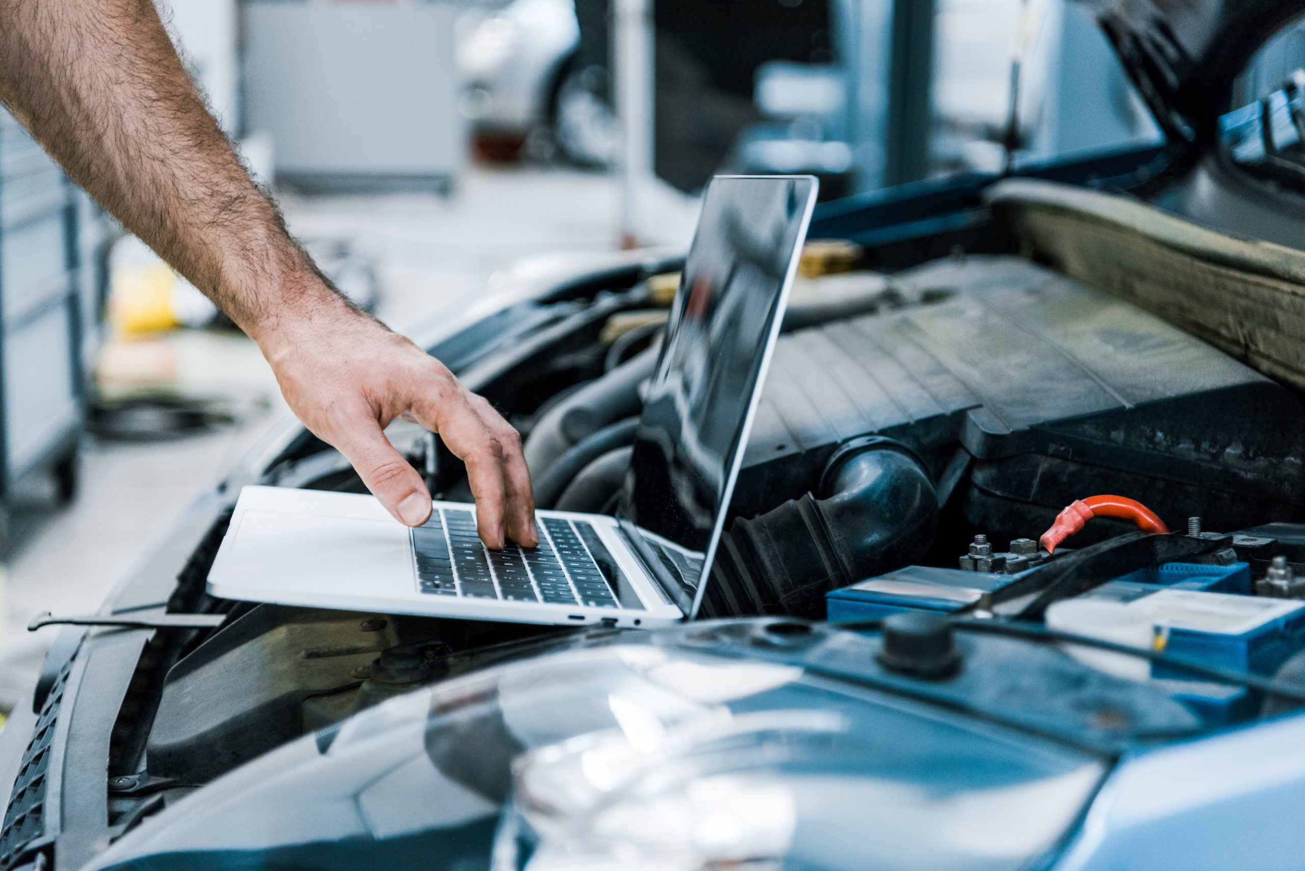 cropped view of auto mechanic using laptop with blank screen near car